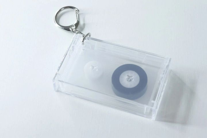 透明なカセットテープ型キーホルダー。中に黒と白のリールが見える