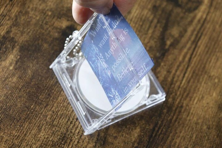 透明なCDケース型キーホルダーに、女性が青い紙を挟み込んでいる
