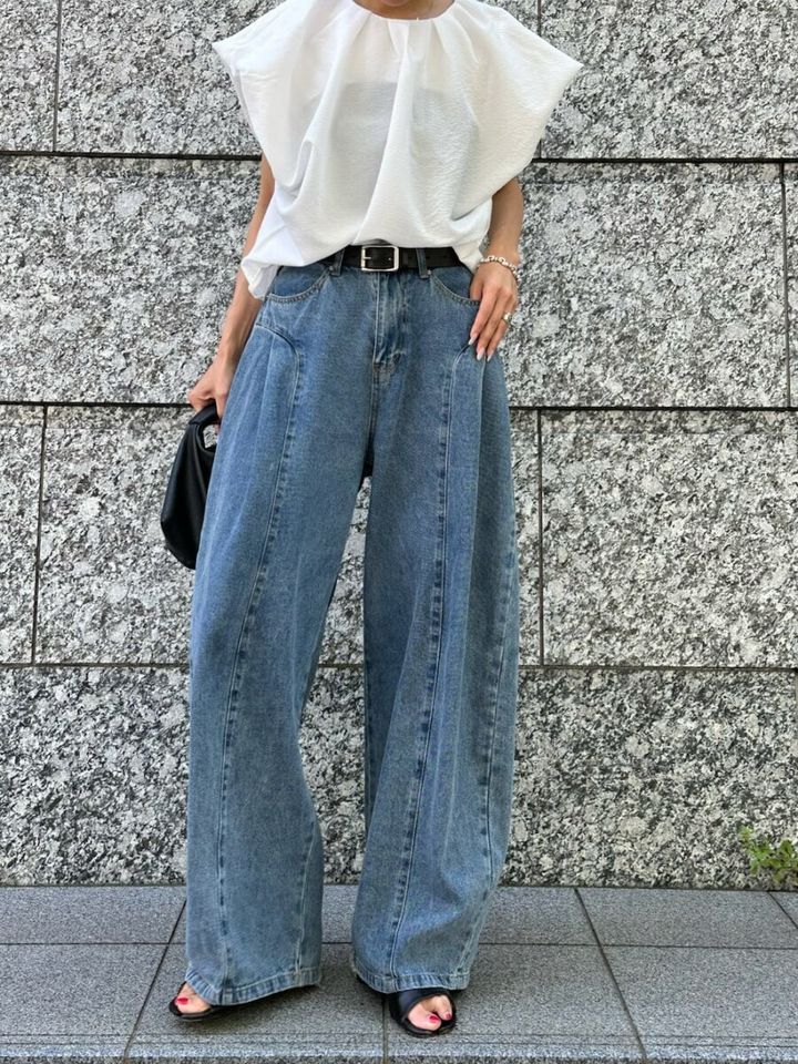 白いギャザーブラウスとワイドデニムを着用し、黒いバッグを持つ女性の全身