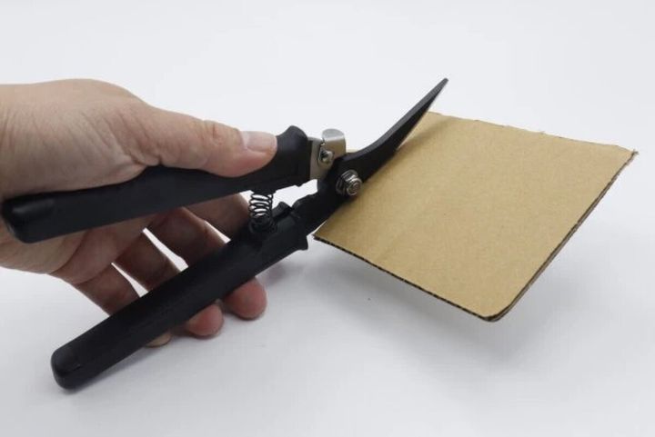 手が黒い万能ハサミで厚手の段ボールを切っている