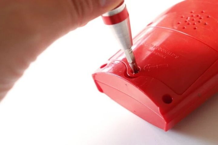 手が赤いペン型精密ドライバーで赤いおもちゃのネジを締めている