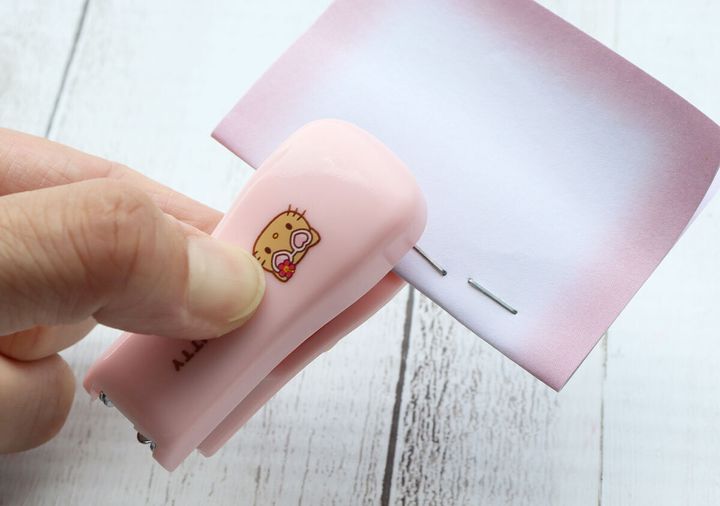 日焼けキティのミニホチキスでピンク色の紙を綴じる手元
