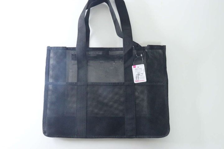 白い背景に置かれた黒いメッシュ素材のトートバッグ。商品タグが付いている。