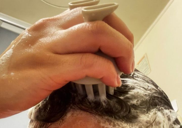 シャンプーブラシを使って髪を洗っている女性の手元