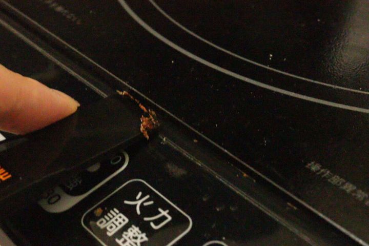 IHクッキングヒーターの隙間にこびりついた焦げ付きを20mm幅のヘラで掻き出している