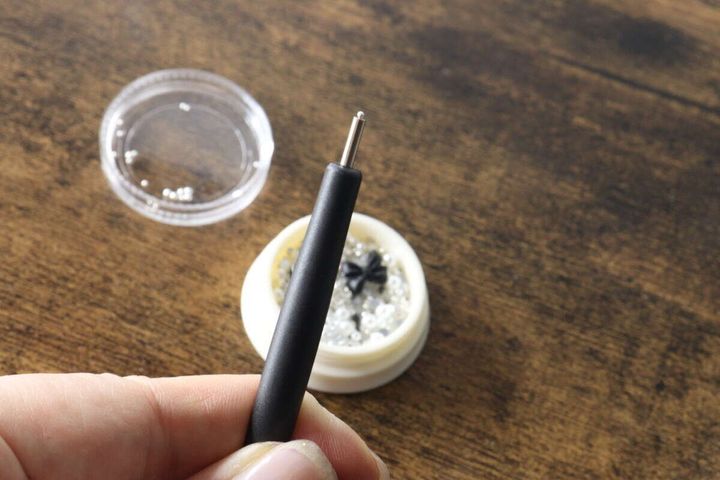 指で持たれたマグネットピックアップペンと、ブリオンが入った容器