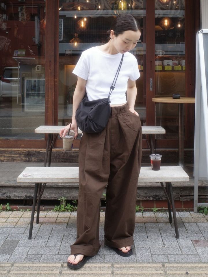 白Tとブラウンワイドパンツの女性がカフェ前で飲み物を持つ