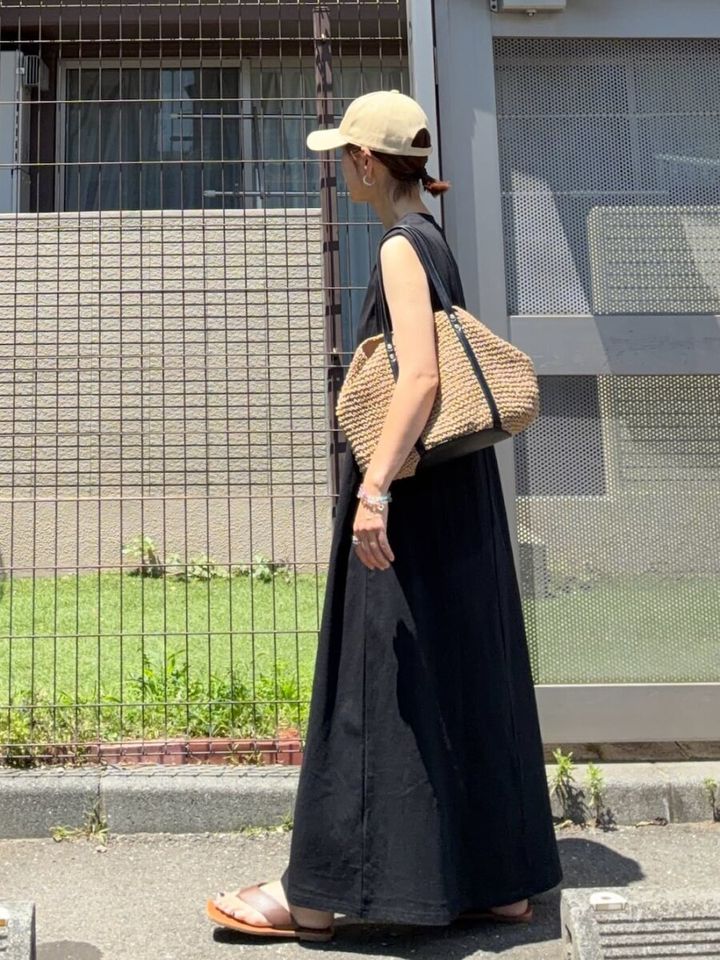 ベージュキャップと黒ワンピの女性がかごバッグを持ち歩く