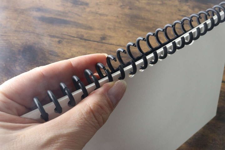 女性の指がルーズリーフにセットされた黒いカラー30リングを開いている