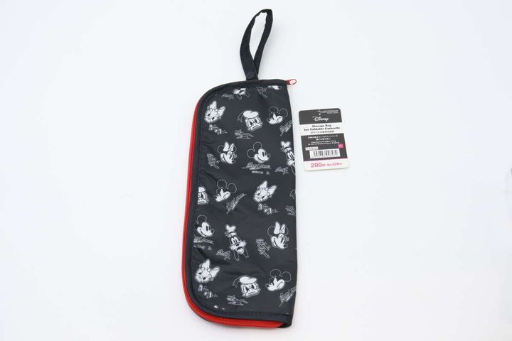 黒い折りたたみ傘用収納袋が白い背景に置かれている。ミッキー＆フレンズの柄で、赤いファスナーとタグが付いている。