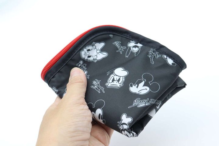 手が折りたたみ傘用収納袋をコンパクトに折りたたんでいる。ミッキー＆フレンズの柄が見える。