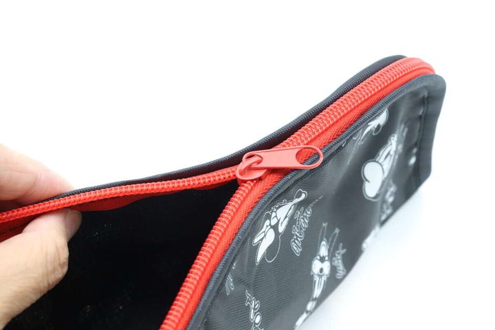 手が折りたたみ傘用収納袋の赤いファスナーを開けている様子。内側の黒い生地が少し見える。