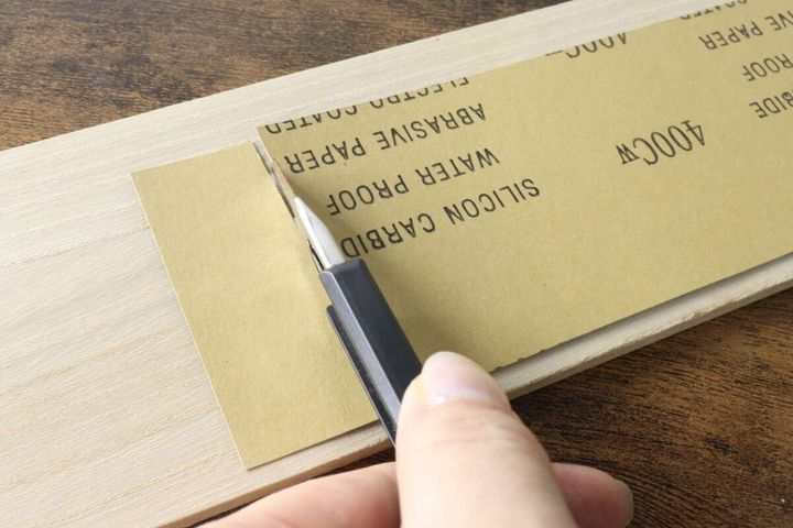 ハサミを使ってサンドペーパーを使いやすい大きさにカットしている手元