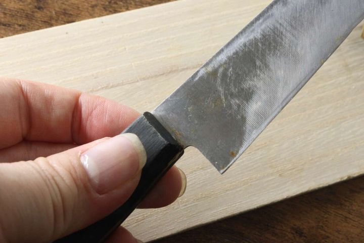 木製のまな板の上に置かれた、刃元にサビが付着した包丁のアップ