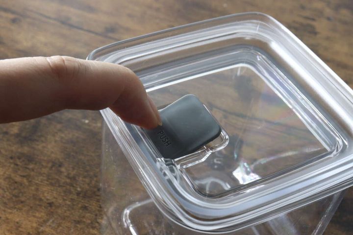 女性の指が密閉容器のフタ中央にあるグレーのプッシュボタンを押している様子