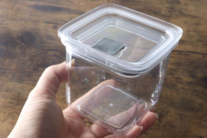 女性の手が透明なワンプッシュ式密閉容器を横から持ち、サイズ感を示している