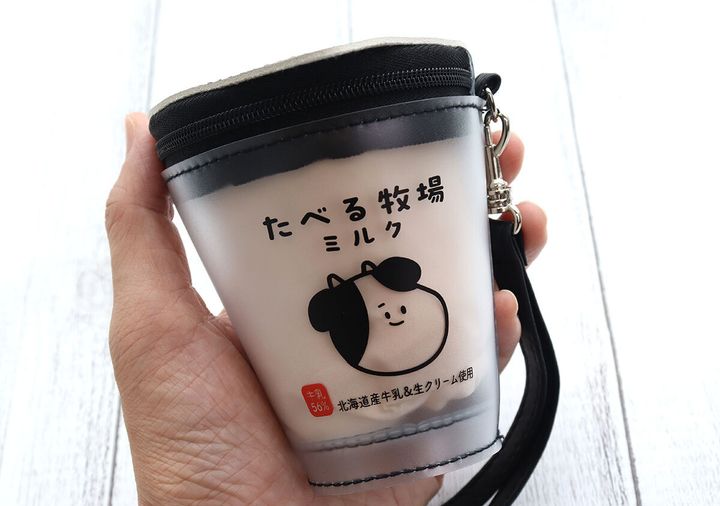 女性がたべる牧場ミルクのカップ型ポーチを手に持っている