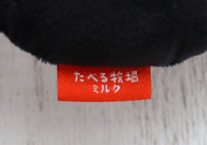 うしフェイスチャームに付いている「たべる牧場ミルク」の赤いロゴタグのアップ