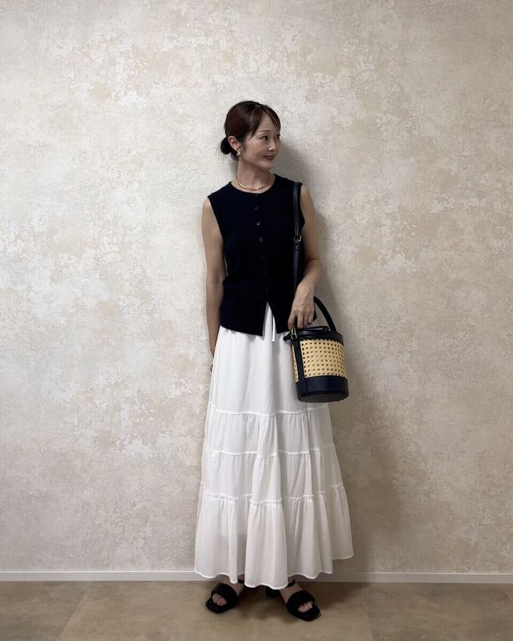黒いノースリーブトップスと白いティアードスカートを着用しカゴバッグを持つ女性