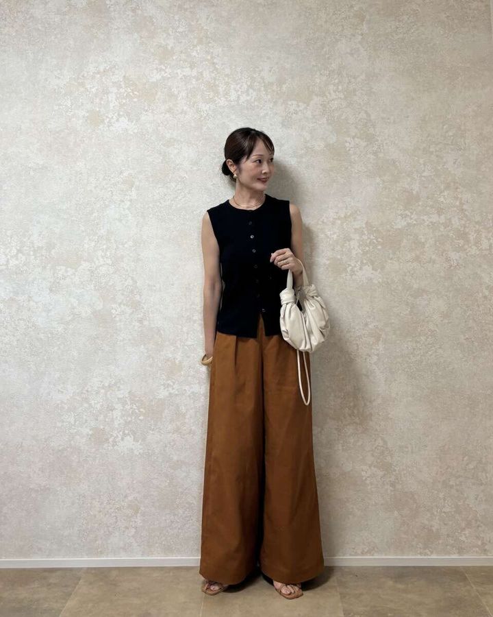黒いノースリーブトップスとブラウンのワイドパンツを着用し白いバッグを持つ女性