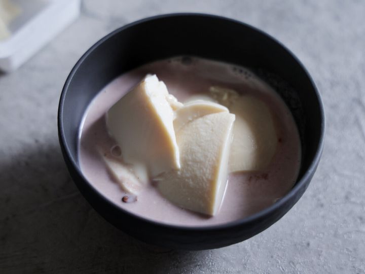 黒い器に入ったココナッツミルクとゆであずきの上に、スプーンですくった絹豆腐を盛り付けている