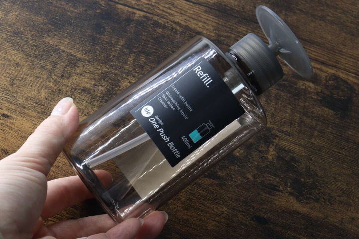 女性の手がアンバー色のワンプッシュボトルを持っている