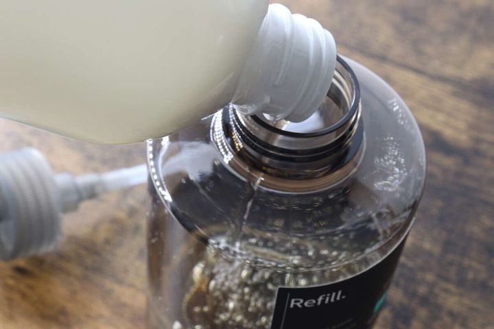 白い洗剤ボトルからワンプッシュボトルに液体を注ぐ様子