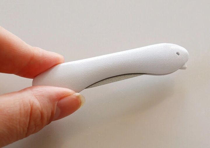 白い折りたたみ爪やすりを指で持っているクローズアップ