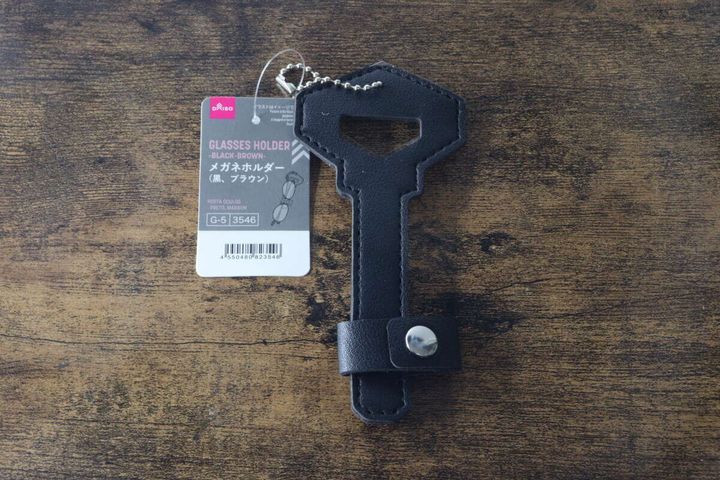 黒い鍵型メガネホルダーが台紙付きで木目調のテーブルに置かれている