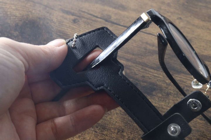 手が黒縁メガネのテンプルを鍵型メガネホルダーの上部ホールに通している