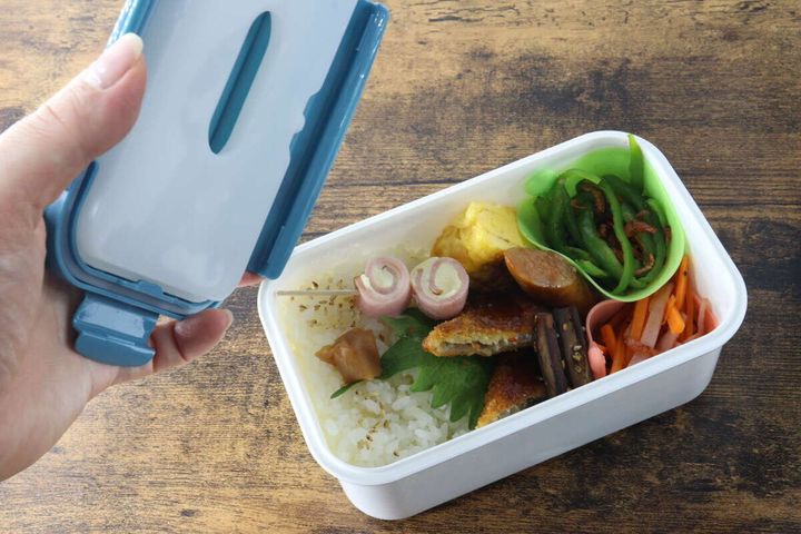 おかずが詰められたお弁当箱に保冷剤付きのフタを閉めようとする手