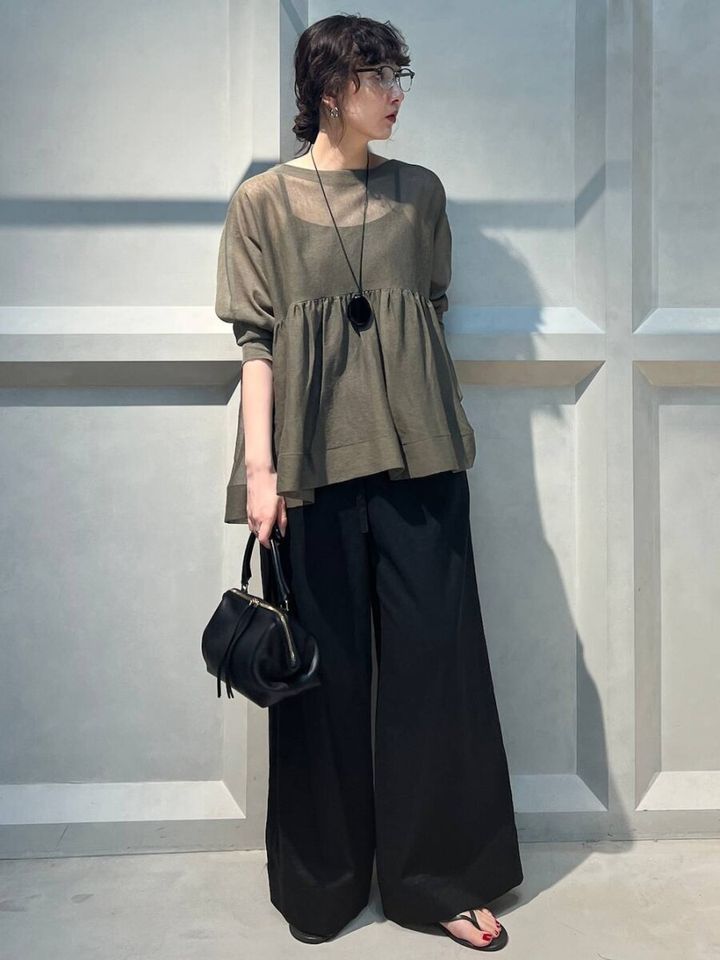 カーキのペプラムシアートップスと黒ワイドパンツ、黒のハンドバッグを持つ女性