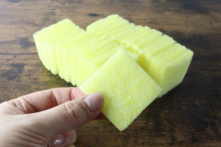 積み重ねられた黄色いクリーナーから女性の手が1枚取り出している様子