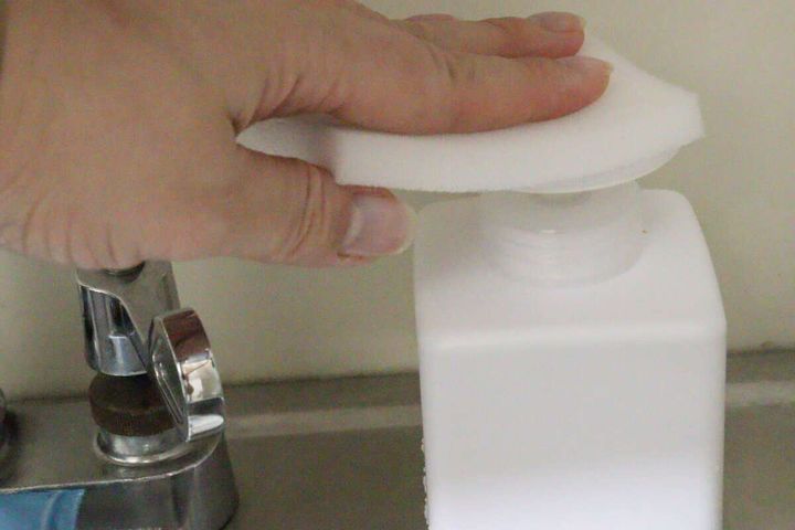 スポンジでワンプッシュディスペンサーのポンプを押す手元