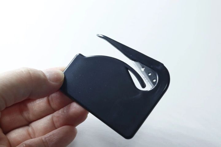 黒いカード型開封カッターを指で持っている