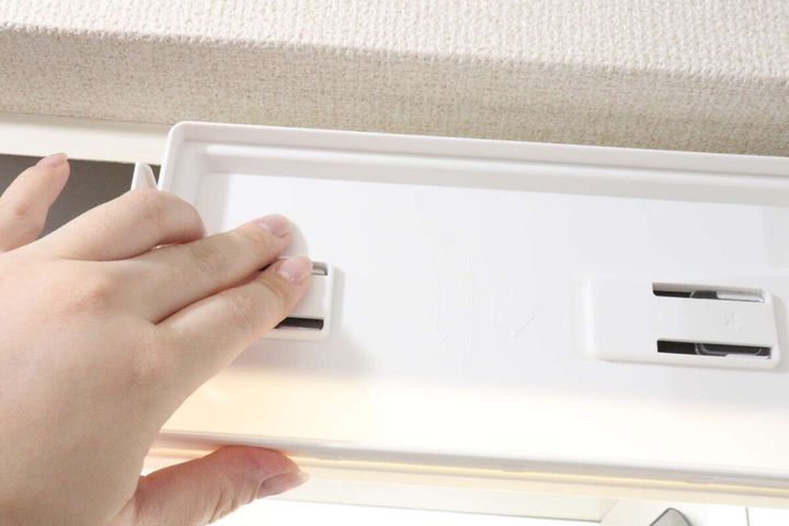 女性の手が「2WAYペーパータオルホルダー」のベースを吊戸棚の下に取り付けている様子。