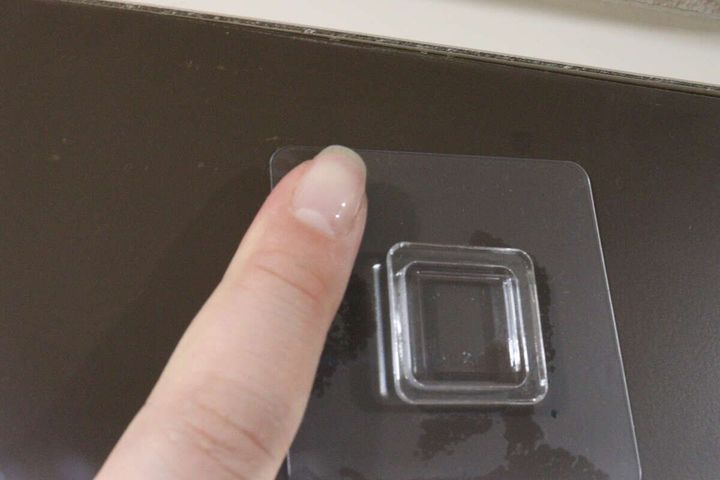 女性の指が、吊戸棚の下に貼り付けた粘着フックをしっかりと押さえつけている様子。