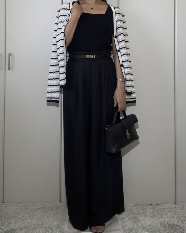 黒いニットインナーとワイドパンツにボーダーカーディガンを羽織りバッグを持つ女性