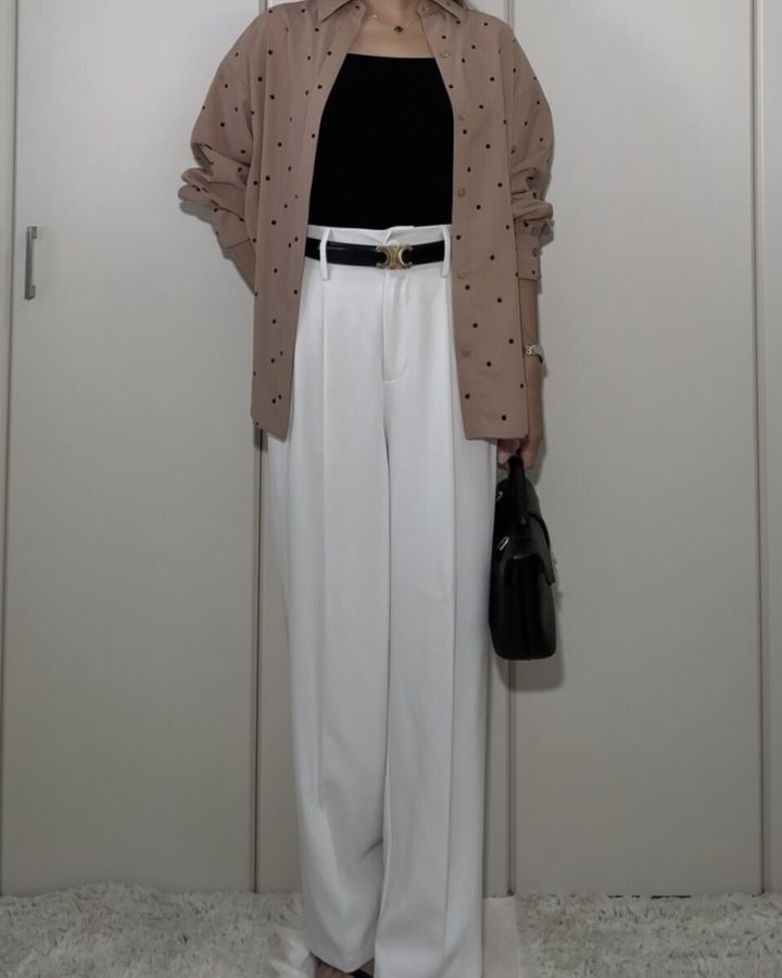 黒いニットインナーと白いワイドパンツにベージュのドット柄シャツを羽織る女性