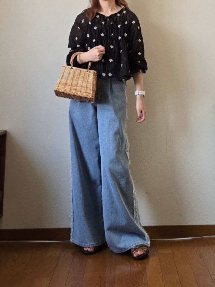 花柄黒ブラウスとライトブルーのワイドデニム、カゴバッグを持つ女性