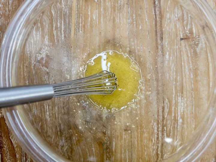 透明なボウルでオリーブオイルなどの調味料を泡立て器で混ぜている俯瞰写真