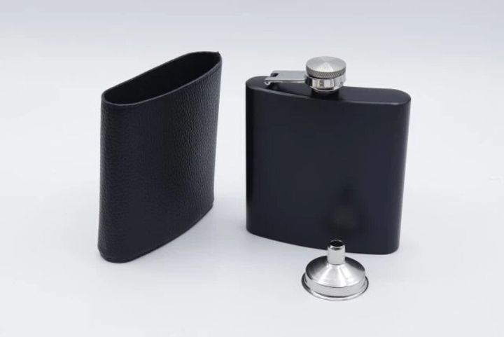 黒いスキットルと革製カバー、注ぎ口の漏斗が並べられている