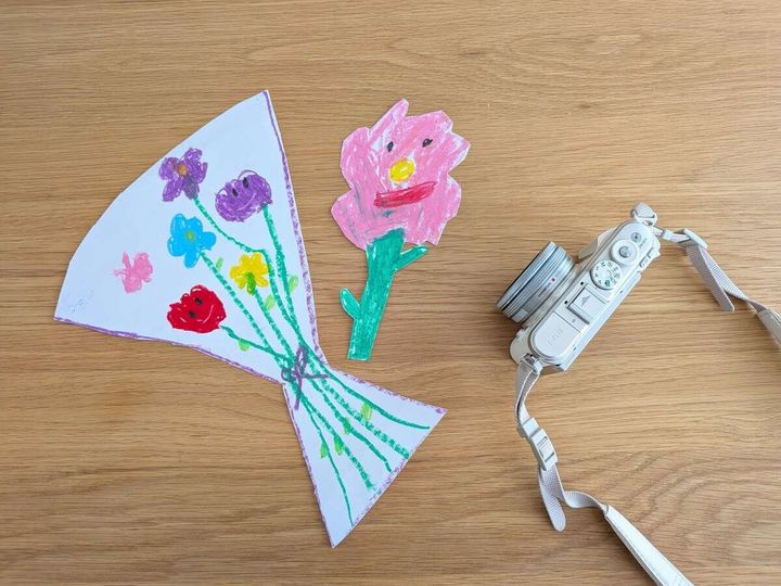 子どもの描いた花の絵と、写真を撮るための白いカメラ