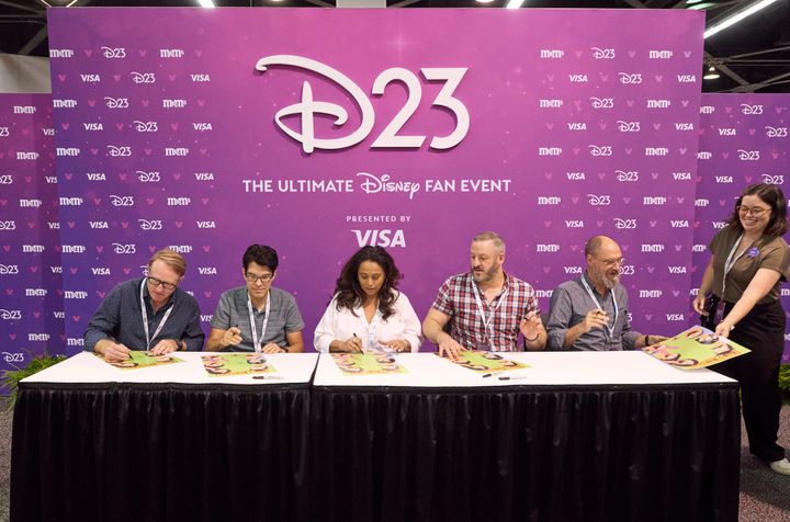 テーブルで色紙にサインする5人とD23のスタッフ