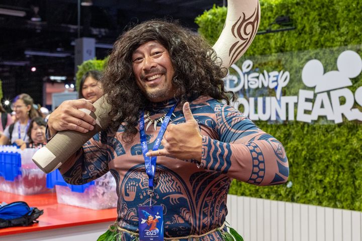 Disney VOLUNTEARSのロゴを背に釣り針のプロップを担いだマウイのコスプレ姿の来場者