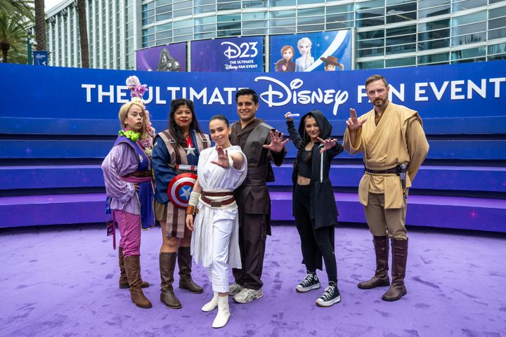 6人のコスプレイヤーが手のひらを前に向けたポーズでバナー前に並ぶ