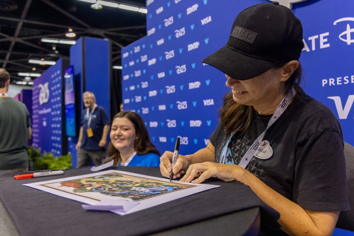 「SHELLY」「IMAGINEER」と記されたネームバッジを着けてサインを書き入れるシェリー・マーティン