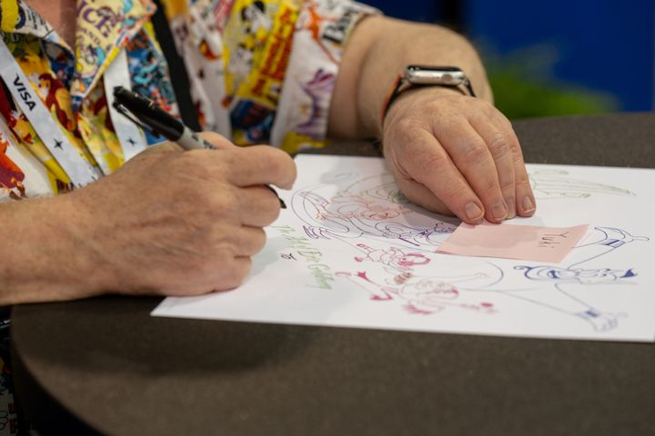 宛名を書いたピンクの付箋が置かれたイラストに、ペンでサインを入れる手元