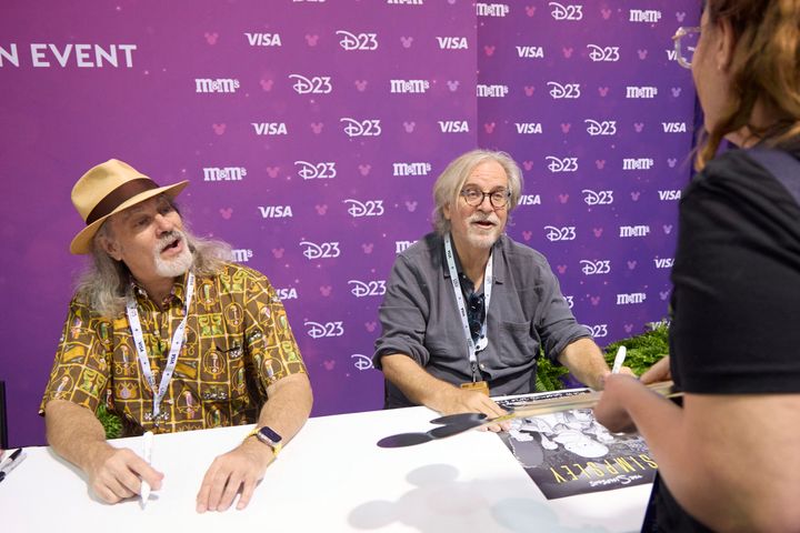 並んで着席し、ファンが差し出したポスターにサインするデヴィッド・シルバーマンとマット・グレイニング