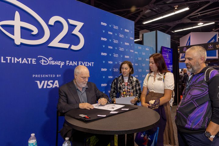 D23のバックドロップを背にサインを書き入れるロン・クレメンツ